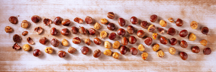 Chestnut panorama. Overhead flat lay panoramic banner with many chestnuts, scattered on a rustic wooden background