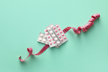 Different pills and measuring tape on color background. Weight loss concept