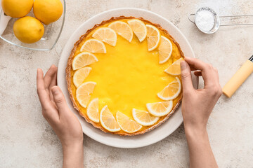 Woman decorating tasty lemon pie on light background