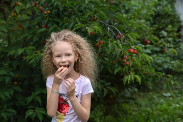 A girl bites a plum ion the garden.Hairstyle after curls
