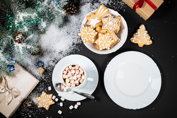 Christmas and New Year decoration composition. Top view of fur-tree branches on dark background with place for your text. Cups of fragrant coffee with marshmallows, gingerbread and chokolate.