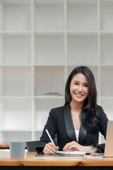Portrait of beautiful asian woman smiling and looking at camera while sitting at office desk.