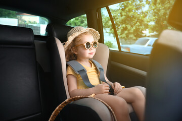 Cute little girl in sunglasses buckled in car safety seat