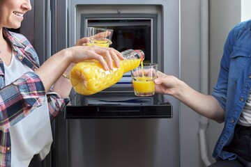 Close up of two womens hands pouring orange juice into glass from refrigerator in kitchen