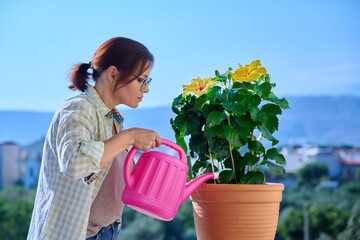 An adult woman watering a flower in a pot from a watering can