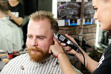 Obraz premium a red-haired adult man is cut by a girl in a barbershop