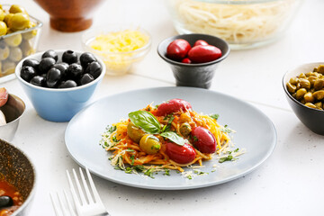 Plate of tasty Pasta Puttanesca and ingredients on white background