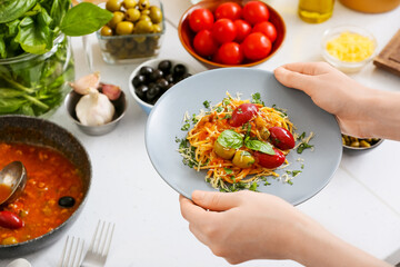 Woman holding plate with tasty Pasta Puttanesca at table