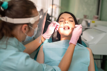 Caucasian female doctor examines the patient's teeth with dental instrument