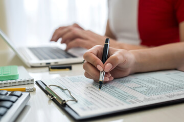 Woman filling US tax form with laptop and calculator at office