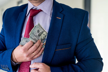 Man in blue suit and red tie putting bribe dollar bills into his pocket