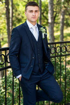 Handsome young groom wearing elegant dark blue suit looking at camera outdoors  portrait. Stylish groom fashion.