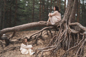 Conceptual photograph of brunettes among forest roots. Beautiful girls sit at the roots of trees...