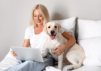 Mature woman with laptop and cute Labrador dog on bed