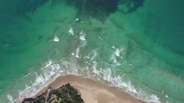 Vertical aerial flight from beach to coral reef in shallow green water