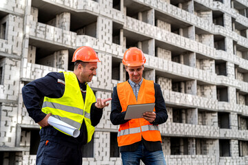 two young smart workers in uniform standing on a construction site discussing a house project