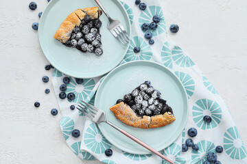 Plates with pieces of tasty blueberry galette on light background