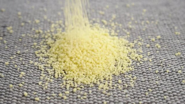 Dry yellow couscous on a rough jute fabric in slow motion. Falling into a heap in slow motion. Close up. Uncooked groats
