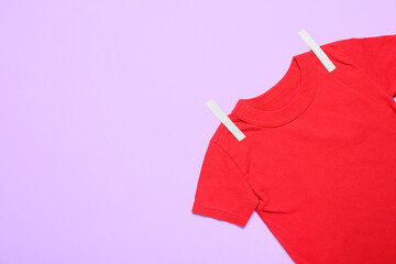 Red t-shirt with paper-cut clothespins on color background, closeup