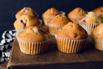 Wooden board with delicious cranberry muffins on table, closeup