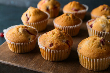 Wooden board with delicious cranberry muffins on table, closeup