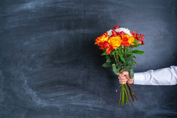 A man's hand holds a bouquet of flowers on the background of a chalk board.