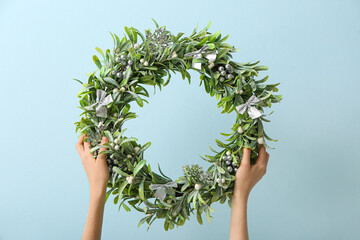 Female hands with beautiful mistletoe wreath on color wall