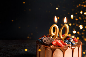 Chocolate birthday cake with berries, cookies and number ninety golden candles on black background,...