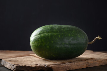 Wax gourd, ash gourd or winter melon on wooden with black background