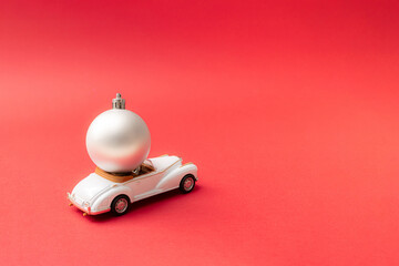 Christmas silver bauble on a luxury white cabriolet limousine. Red pastel background. New year...