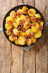 German fried potatoes with bacon and onions close-up in a plate on the table. vertical top view from above