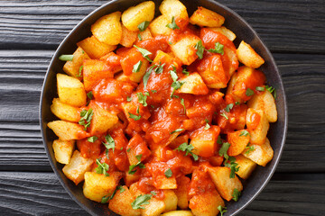 Spanish Patatas bravas it typically consists of white fried potatoes and served warm with a spicy sauce close up in the plate on the table. Horizontal top view from above