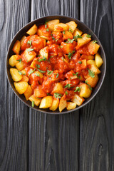 Patatas Bravas are crispy golden potatoes topped with a spicy red sauce close up in the plate on the table. Vertical top view from above