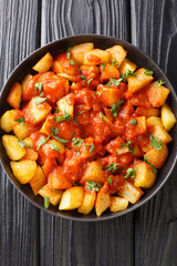 Patatas Bravas is a classic Spanish dish of fried potato cubes served with a spicy dipping sauce close up in the plate on the table. Vertical top view from above