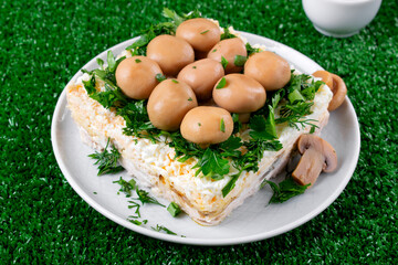 Layered salad with chicken, cheese, eggs and fried mushrooms topped with pickled champignons and herbs reminding a clearing