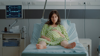 Portrait of pregnant person sitting in hospital ward bed with monitor preparing for child delivery at clinic. Caucasian young woman feeling impatient expecting labor contractions