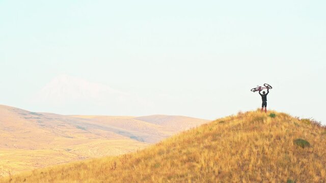 Isolated fit young caucasian male person lift bicycle up on hill with mountains background outdoors in caucasus mountains. Achievement , inspiration, challenge and determination concept - Powered by Adobe