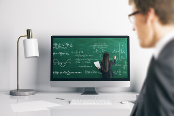 Young businessman at office desk looking at computer screen with online education chalkboard and formulas pattern. Digital knowledge and webinar concept.