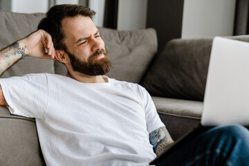 Bearded european man working with laptop while sitting on floor