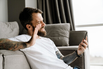 Bearded european man using mobile phone while sitting on floor