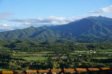 Landscape in south of france viewed from rooftop featuring green fields, houses and trees against backdrop of Canigou, a sacred mountain to Catalan people