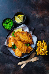 Fish and chips with green peas on dark background. British cuisine concept.