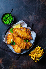 Fish and chips with green peas on dark background. British cuisine concept.