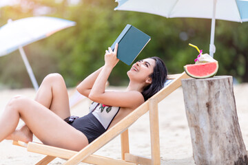 attractive girl in white bikini with book on beach chair near sea