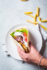 Hand hold chicken gyros with vegetables, french fries and tzatziki sauce. Greek food concept.