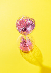 hourglass with pink sparkling sequins on a yellow background with hard lights and shadows