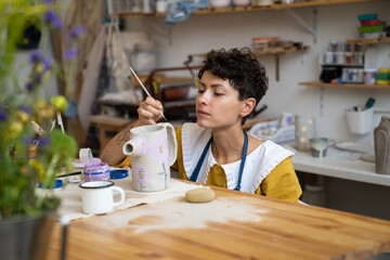 Creative process in pottery studio: young craftswoman or self employed ceramist decorating potter...