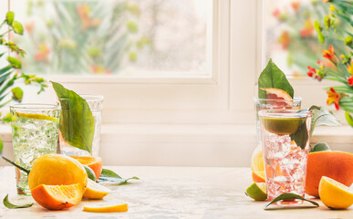 Iced citrus drinks with mint, orange and grapefruit on kitchen table at window with natural light....