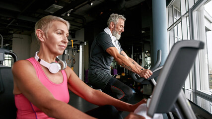 Senior couple doing cardio exercise on bikes in gym