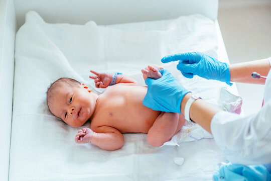 Unrecognizable pediatrician hands in blue gloves check feet of newborn baby in hospital.